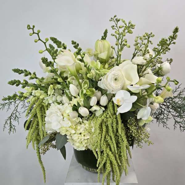 White floral arrangement with calla lilies, orchids, and trailing green accents in a vase