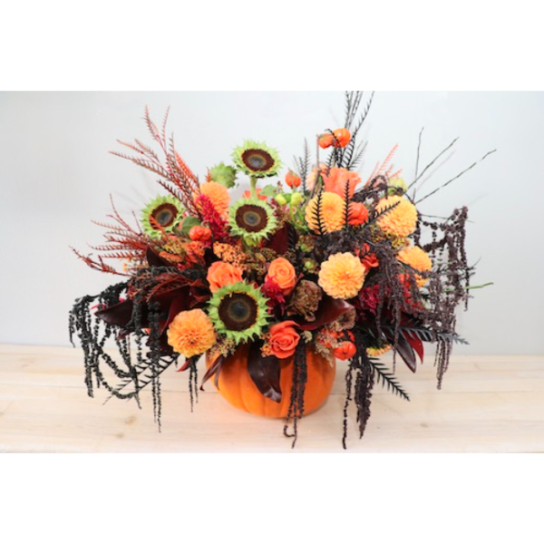 Orange and black floral arrangement in a pumpkin-shaped container