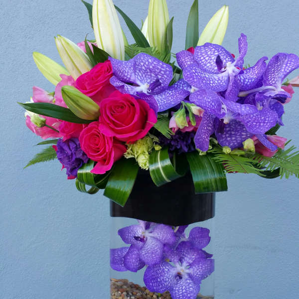 Bouquet of pink roses, lilies, and purple orchids in a glass vase
