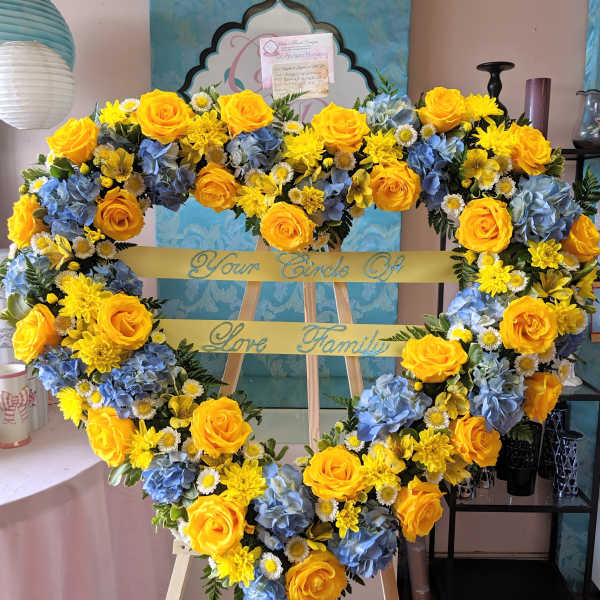 Heart-shaped floral wreath with yellow roses, blue hydrangeas, and daisies on an easel