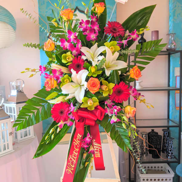 Tall standing floral spray with lilies, gerbera daisies, roses, and orchids on an easel