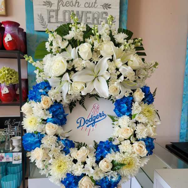 Large floral wreath with white lilies, roses, and blue hydrangeas around a Dodgers logo