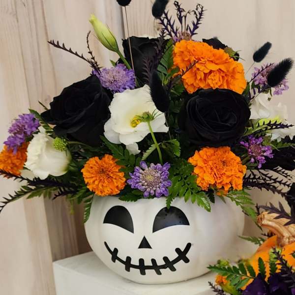 Halloween flower arrangement in a jack-o'-lantern container with black, orange, white, and purple blooms.