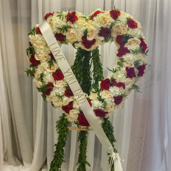 Heart-shaped rose wreath with a memorial ribbon on a stand