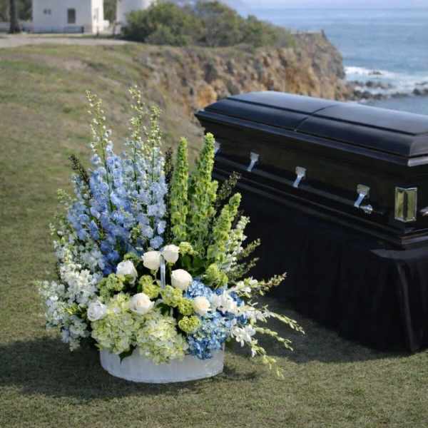 White and blue funeral flowers beside a black casket outdoors