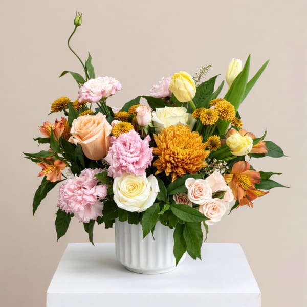 Mixed bouquet of roses, carnations, and mums in a white vase