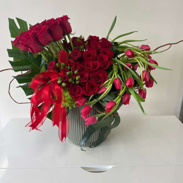 Red roses and pink tulips arranged in a ribbed vase with a red ribbon