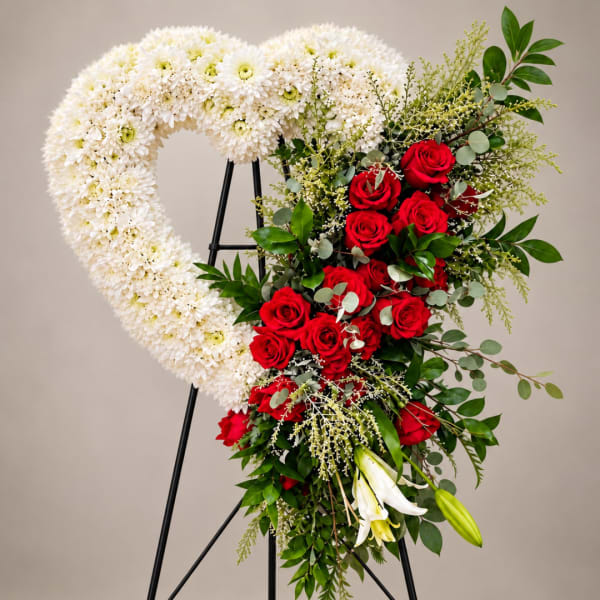 Heart-shaped floral wreath with white chrysanthemums and red roses on a stand