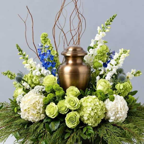 Green and white floral arrangement around a bronze urn with blue accents