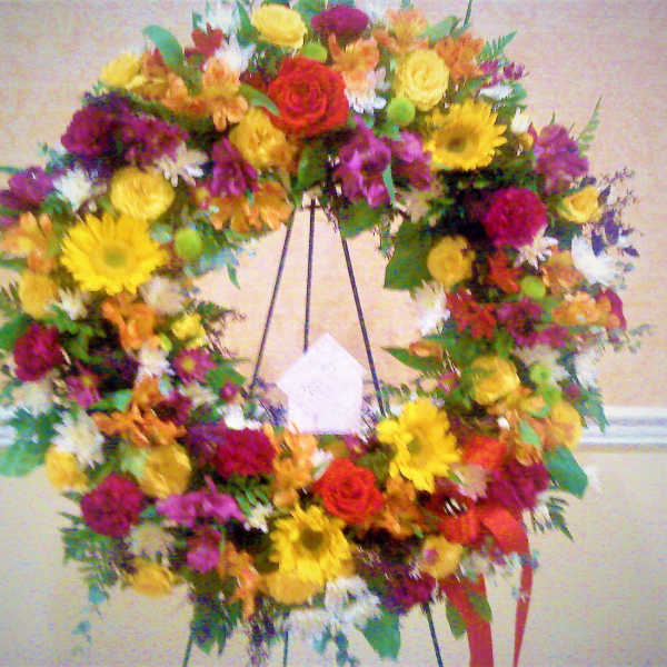 Large mixed flower wreath on a black stand with bright yellow, red, purple, and white blooms
