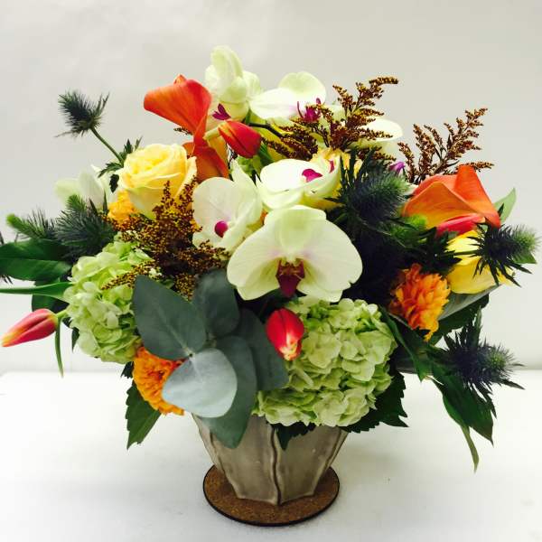 Mixed bouquet with orchids, roses, hydrangeas, and orange calla lilies in a metal vase