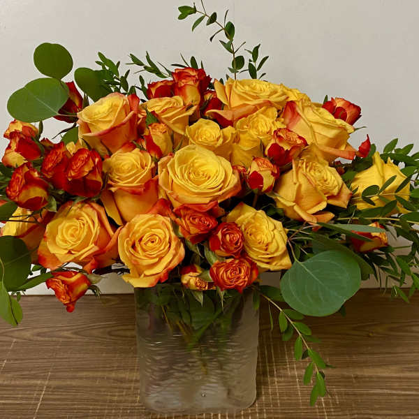 Yellow and orange roses arranged in a clear glass vase
