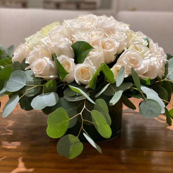 Low arrangement of ivory roses in a round vase with a collar of eucalyptus.