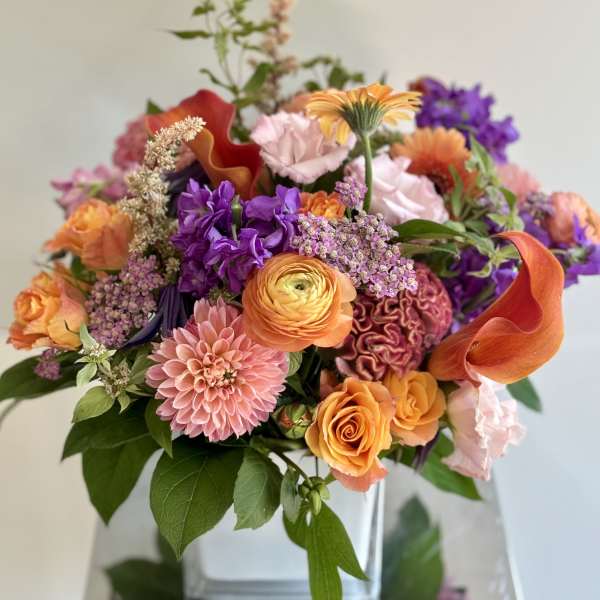 Colorful mixed bouquet with orange, pink, and purple flowers in a clear vase