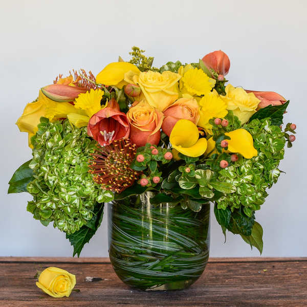 Yellow and peach floral arrangement in a glass vase with hydrangeas and roses