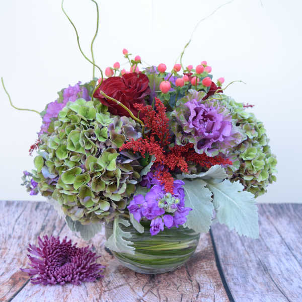 Mixed bouquet with hydrangeas, roses, and purple blooms in a glass vase