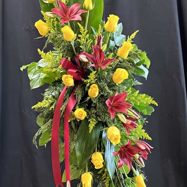 Tall floral spray with yellow roses and burgundy lilies on a stand