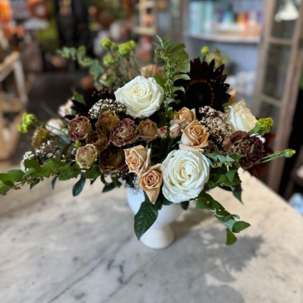White and tan roses arranged in a white vase with greenery