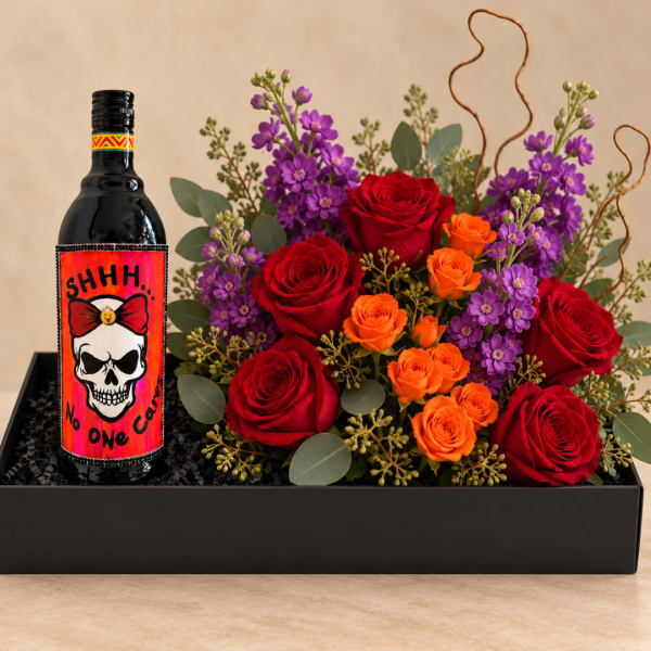 Red and orange roses with purple flowers in a black gift box beside a decorated bottle