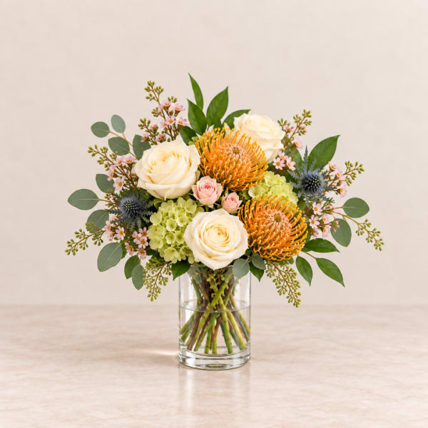 Bouquet of cream roses, orange pincushion blooms, and pink flowers in a glass vase