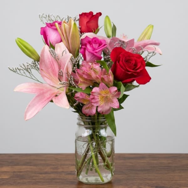 Pink and red bouquet with lilies, roses, and alstroemeria in a glass jar