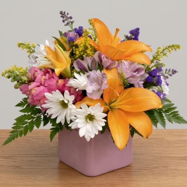 Mixed bouquet with orange lilies, white daisies, and pink flowers in a pink vase