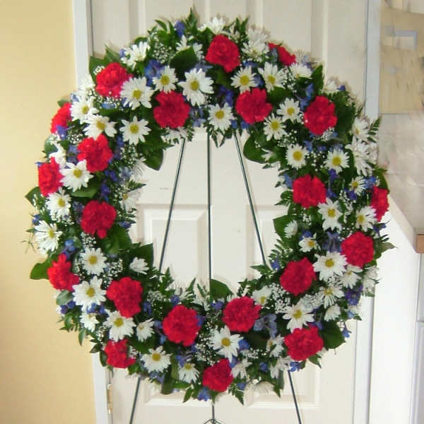Circular floral wreath with red carnations and white daisies on a stand
