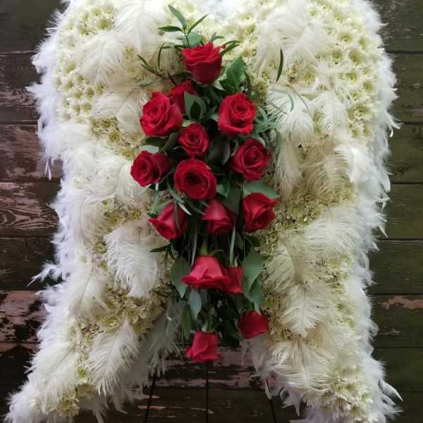 Standing funeral spray of red roses on a white feathered wreath