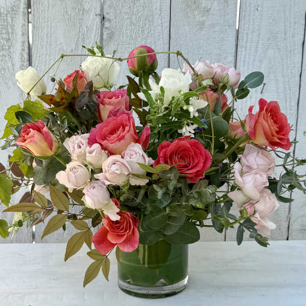 Mixed pink, coral, and white roses arranged in a glass vase