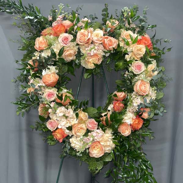 Heart-shaped floral wreath with peach and pink roses on a stand