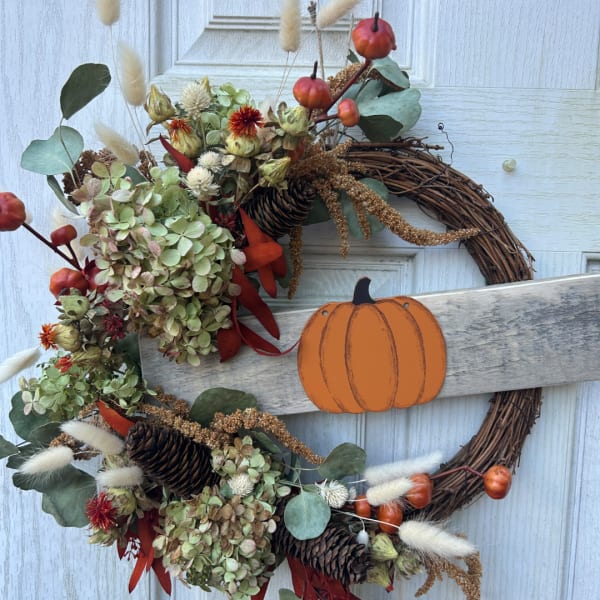 Fall wreath with dried flowers, pinecones, and a pumpkin sign on a white door