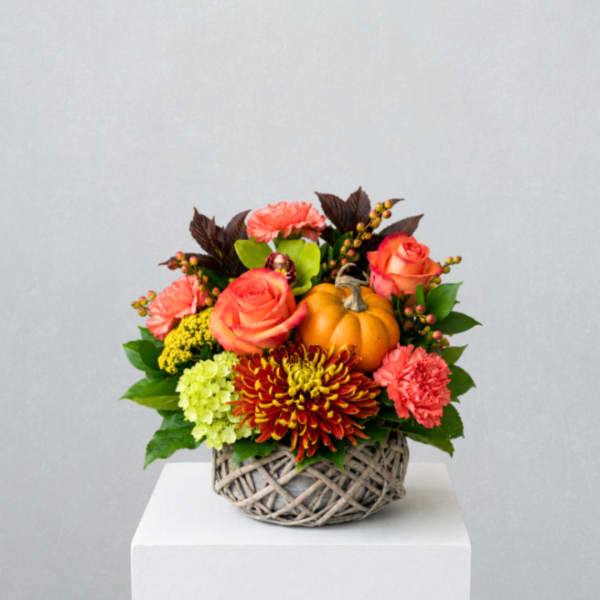 Autumn floral arrangement in a woven basket with a small pumpkin