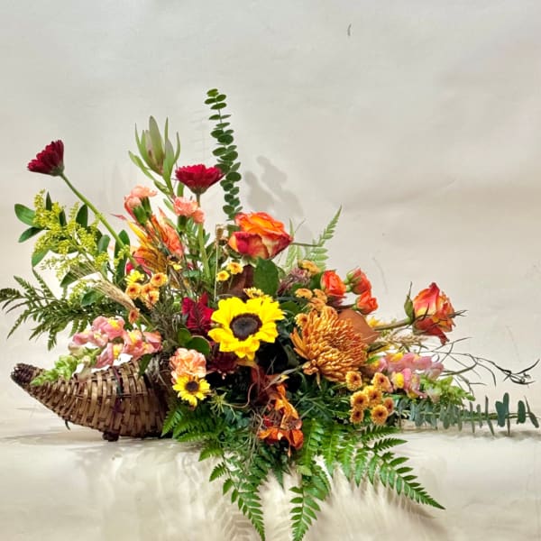 Mixed floral arrangement in a woven basket with bright orange, yellow, pink, and burgundy blooms