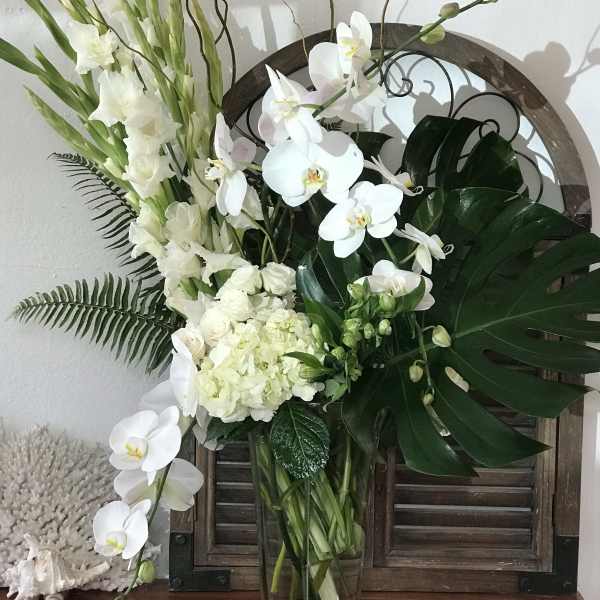 White orchids and gladiolus arranged in a clear glass vase