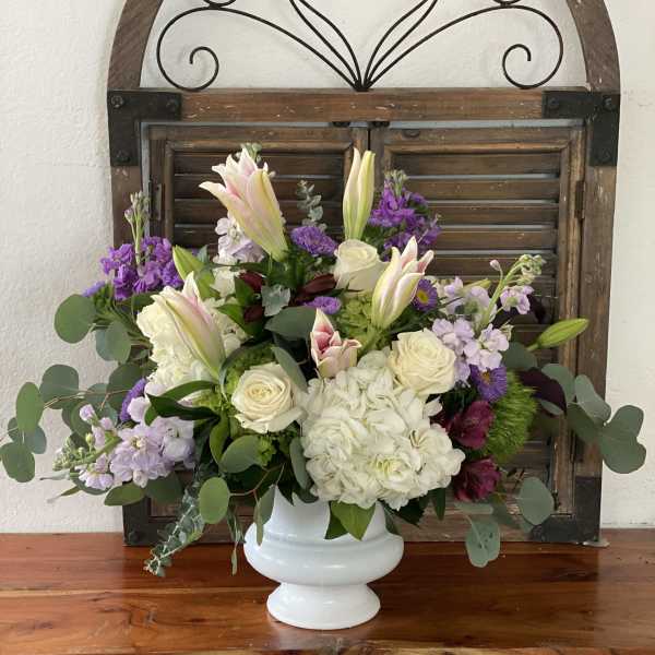 White vase arrangement with lilies, roses, hydrangea, and purple flowers