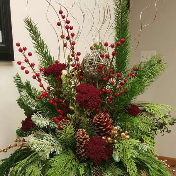 Tall holiday arrangement with red berries, pine, and pinecones in a silver vase