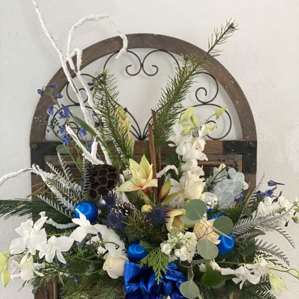 Holiday floral arrangement in a silver vase with blue ribbon and white blooms