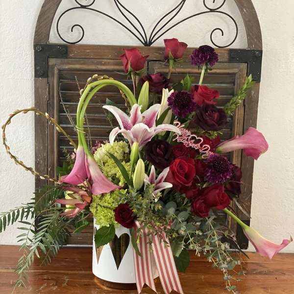 Mixed bouquet of red roses, pink lilies, and purple blooms in a white container