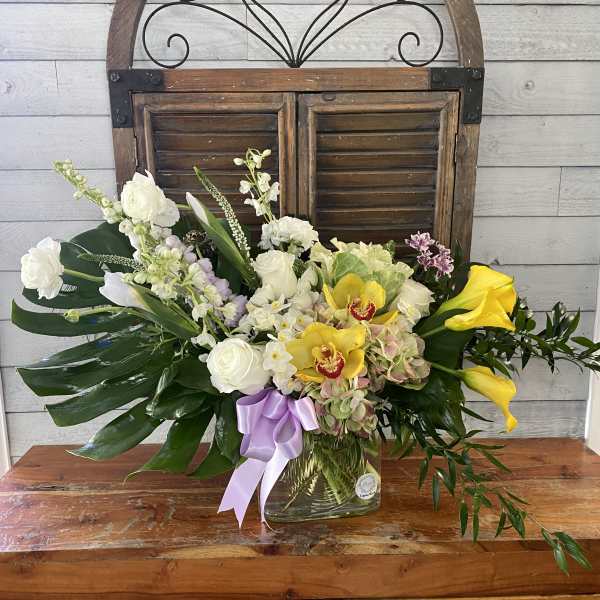Mixed floral arrangement in a glass vase with white, yellow, and lavender blooms