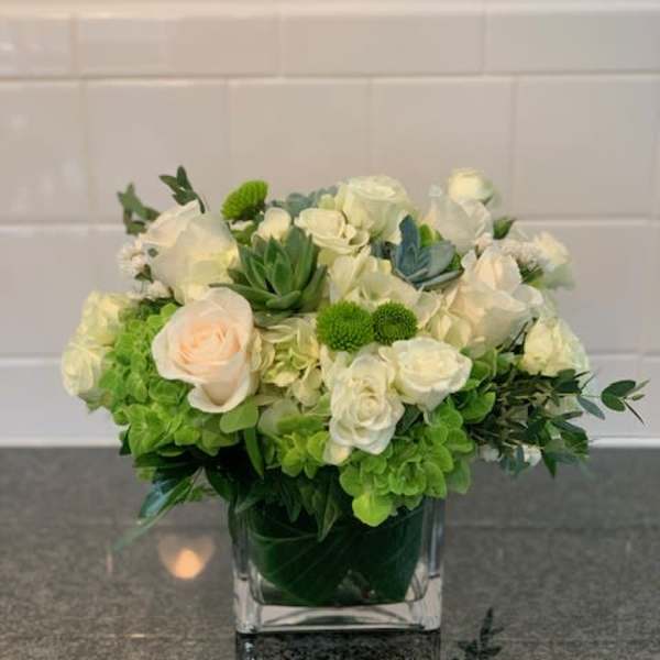 White and green floral arrangement in a square glass vase
