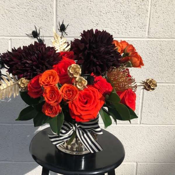 Red and orange rose arrangement in a silver vase with a striped ribbon