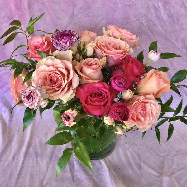 Pink and peach roses in a glass vase with purple flowers