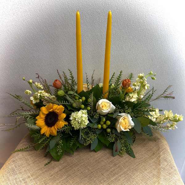 Floral centerpiece with two tall yellow candles and sunflowers in a low arrangement