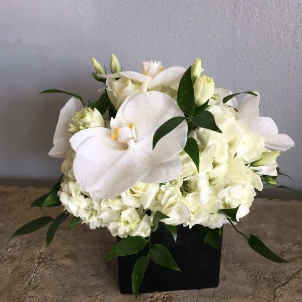 White floral arrangement with calla lilies and hydrangeas in a black container