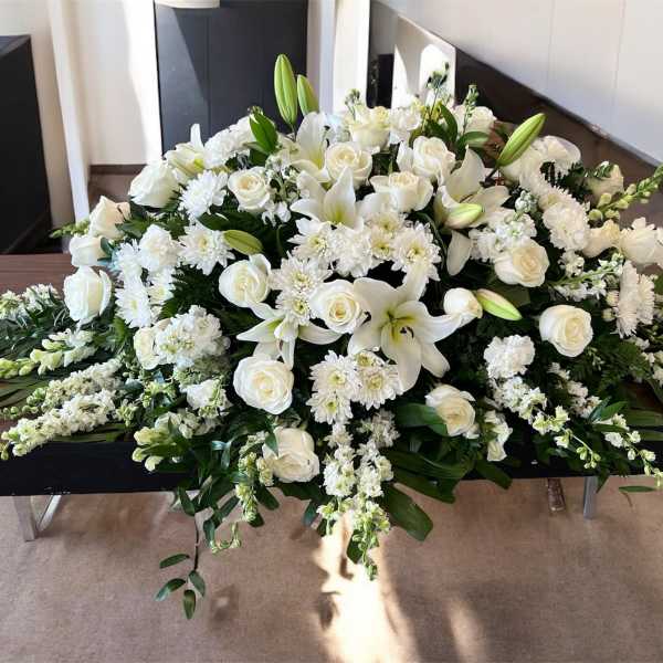 White floral casket spray with roses, lilies, and chrysanthemums