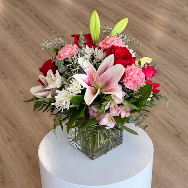 Mixed bouquet in a clear square vase with pink lilies, red roses, and carnations