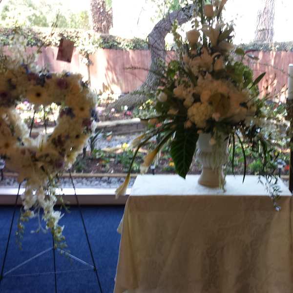 Heart-shaped floral wreaths on stands flank a white vase arrangement on a table.