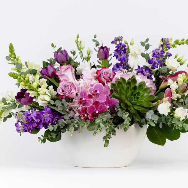 Mixed purple and white floral arrangement in a white bowl vase