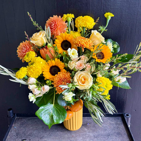 Mixed bouquet with sunflowers, roses, and orange blooms in a yellow vase