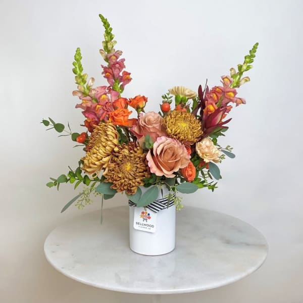 Mixed bouquet in a white vase with orange, pink, and gold blooms